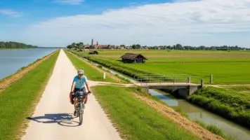 Ciclista lungo l'Anello di Adria con vista sui paesaggi fluviali del Delta